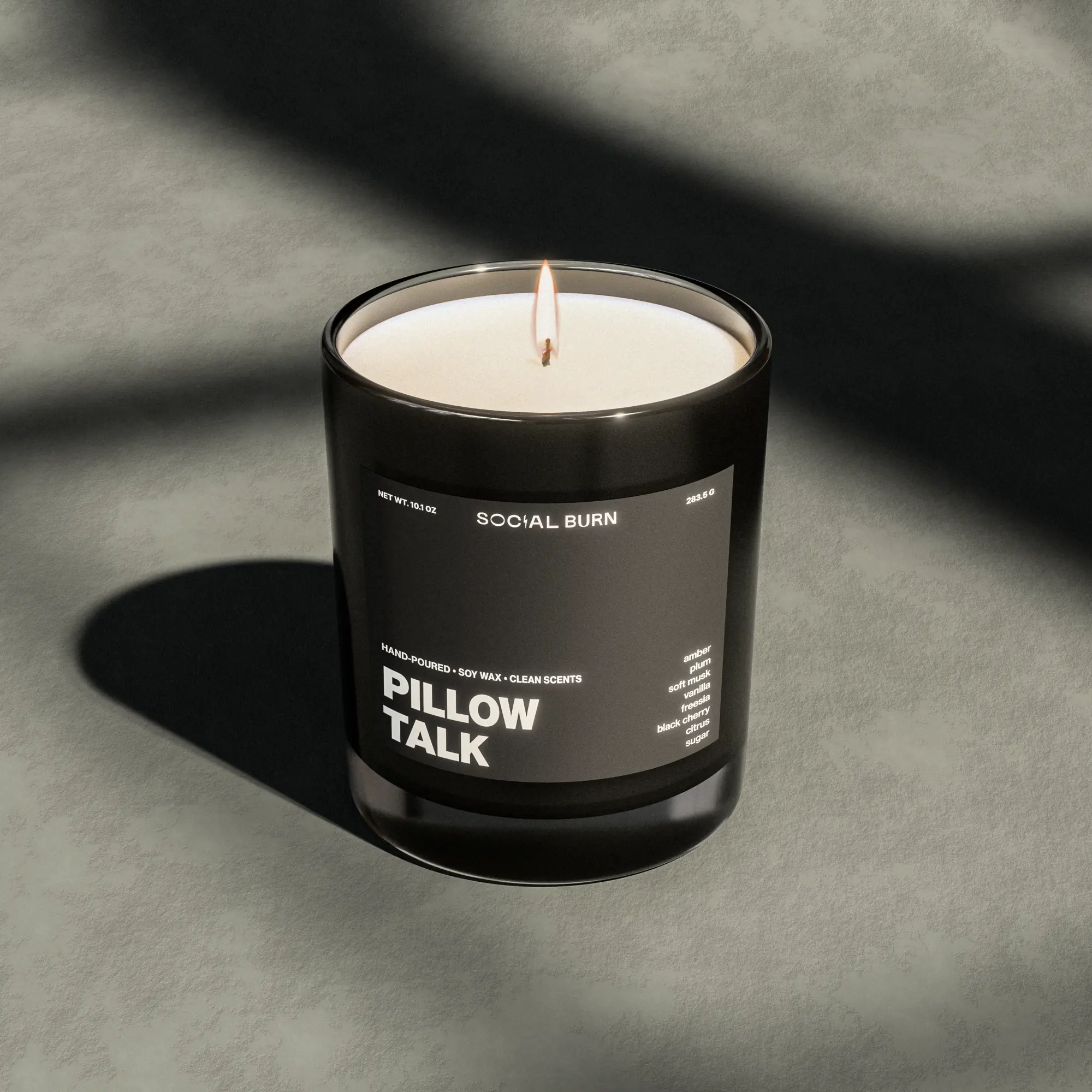 Lit candle in a dark glass with window shadows